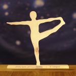 Postura de yoga "el canguro" en madera, sobre base de madera con nombre en sánscrito y en castellano.