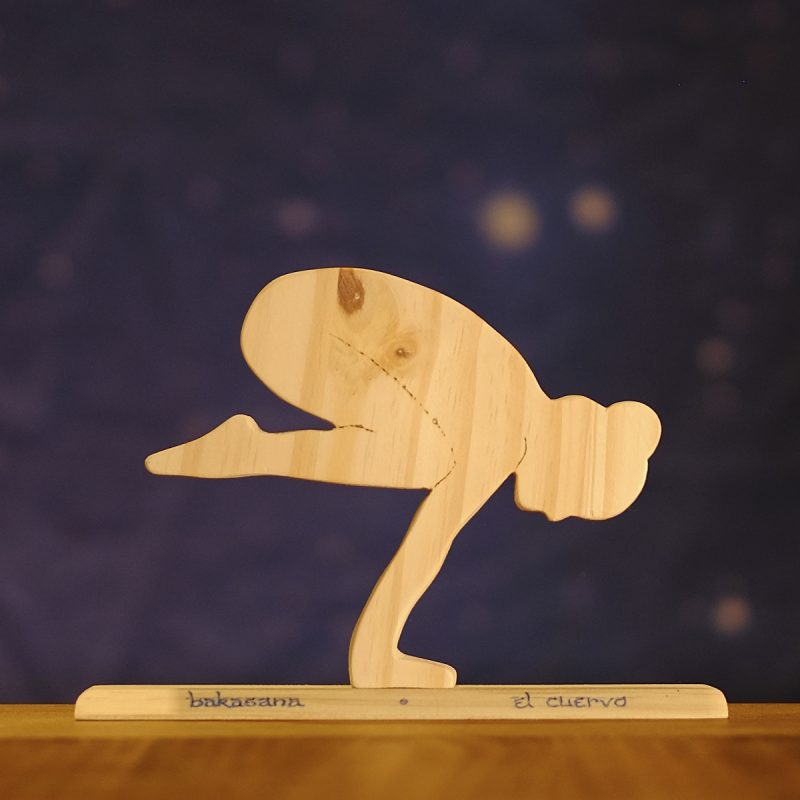Postura de yoga el cuervo, en madera sobre base con nombre en sánscrito y en castellano