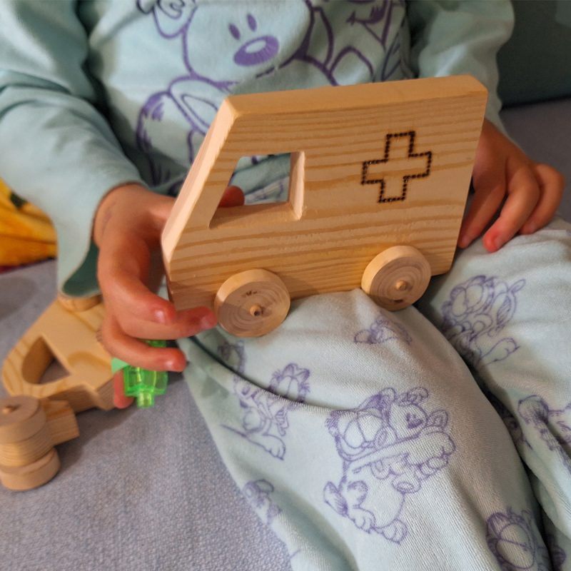 Ambulancia de madera, juguete en manos de una niña de 4 años