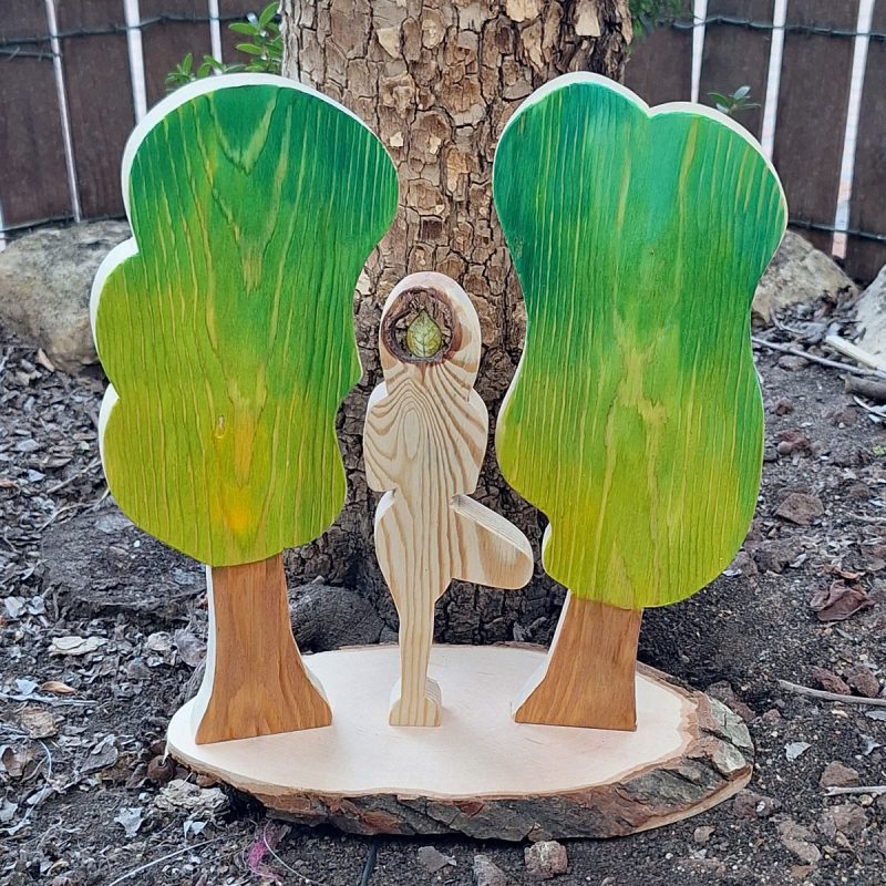 Asana de yoga El Árbol, de madera, con dos árboles a los lados y sobre una rueda de madera